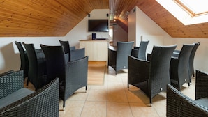 A high-ceilinged room with wooden beams, a dining area with wicker furniture, and a TV mounted on the wall. - Spacious Retreat by Lake (Waimes)