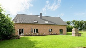 A single-story brick building with a tiled roof, a small porch with chairs, and a well-maintained lawn. - Spacious Retreat by Lake (Waimes)