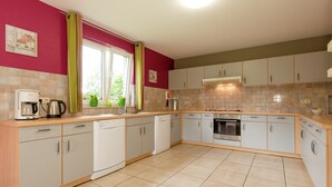 A kitchen with white cabinets, a coffee maker, and a window with curtains. - Spacious Retreat by Lake (Waimes)