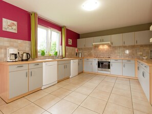 A kitchen with white cabinets, a coffee maker, and a window with curtains.