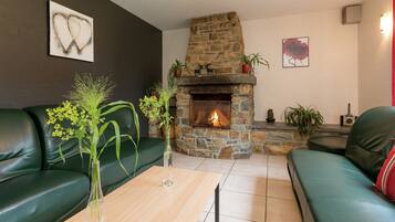 A living room with a stone fireplace, green leather sofas, a wooden coffee table, and decorative plants.