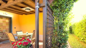 A patio with a table and chairs, a potted plant with red flowers, and a wooden fence. - Belvilla by OYO Montebello Bilo A (Bolano)