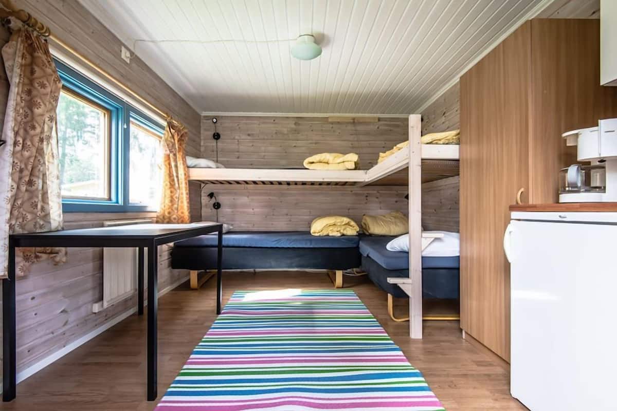 A compact cabin with bunk beds, a small kitchenette, and a window with curtains.
