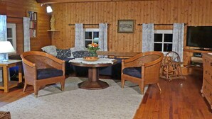 A cozy cabin interior with a wooden ceiling, a sofa, two wicker chairs, a small table with a vase of flowers, a television, and a wooden dresser. - Chalet in Kollnburg Near St. Englmar Ski Area (Kollnburg)