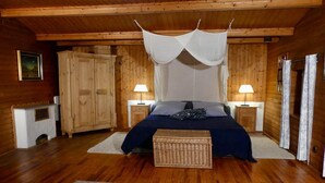 A wooden cabin bedroom with a bed, two bedside tables with lamps, a chest of drawers, and a fireplace. - Chalet in Kollnburg Near St. Englmar Ski Area (Kollnburg)