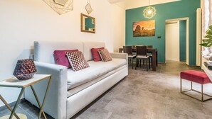 A modern living room with a sofa, dining table, and chairs. There are decorative mirrors and a painting on the wall.