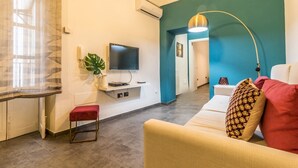 A modern living room with a flat-screen TV, a red bench, a sofa with patterned cushions, and a teal accent wall.