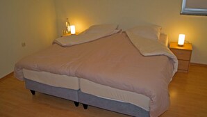 Un lit avec une couette de couleur claire, une table de chevet avec une lampe et un plancher en bois.