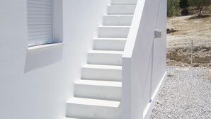 A white staircase leading to a door, with a window and a view of trees and a fence in the background. - Stylish Villa in Loutra with Private Pool & Garden near Sea Beach (Rethymno)