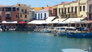 A harbor with boats docked, a waterfront restaurant with outdoor seating, and buildings with balconies. - Stylish Villa in Loutra with Private Pool & Garden near Sea Beach (Rethymno)