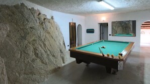 Une table de billard dans une pièce dont le mur est recouvert d’un revêtement texturé et où l’on trouve également un miroir.