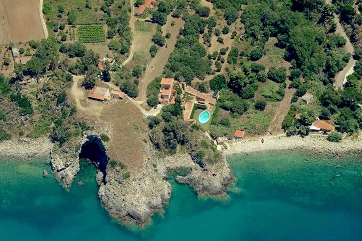 Vue aérienne d’une propriété située sur la côte, avec un rivage rocheux, une piscine et un petit bâtiment.