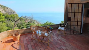 Une terrasse dotée de chaises et d’une table en osier, offrant une vue imprenable sur le paysage côtier et la mer.