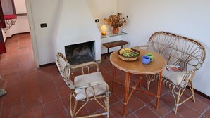 Une pièce chaleureuse avec une cheminée, des fauteuils en osier, une table ronde et un sol carrelé.