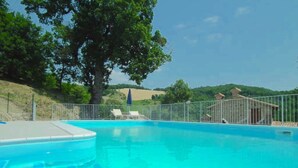A swimming pool with a metal fence, lounge chairs, and a tree in the background. - Farmhouse in Marche With Pool and Views (Mercatello sul Metauro)