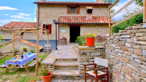 A rustic stone building with a tiled roof, a wooden pergola, and a table set for dining. - Farmhouse in Marche With Pool and Views (Mercatello sul Metauro)