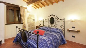 A bedroom with a stone wall, a bed with a metal frame, a wooden ceiling, and a window with curtains. - Farmhouse in Marche With Pool and Views (Mercatello sul Metauro)
