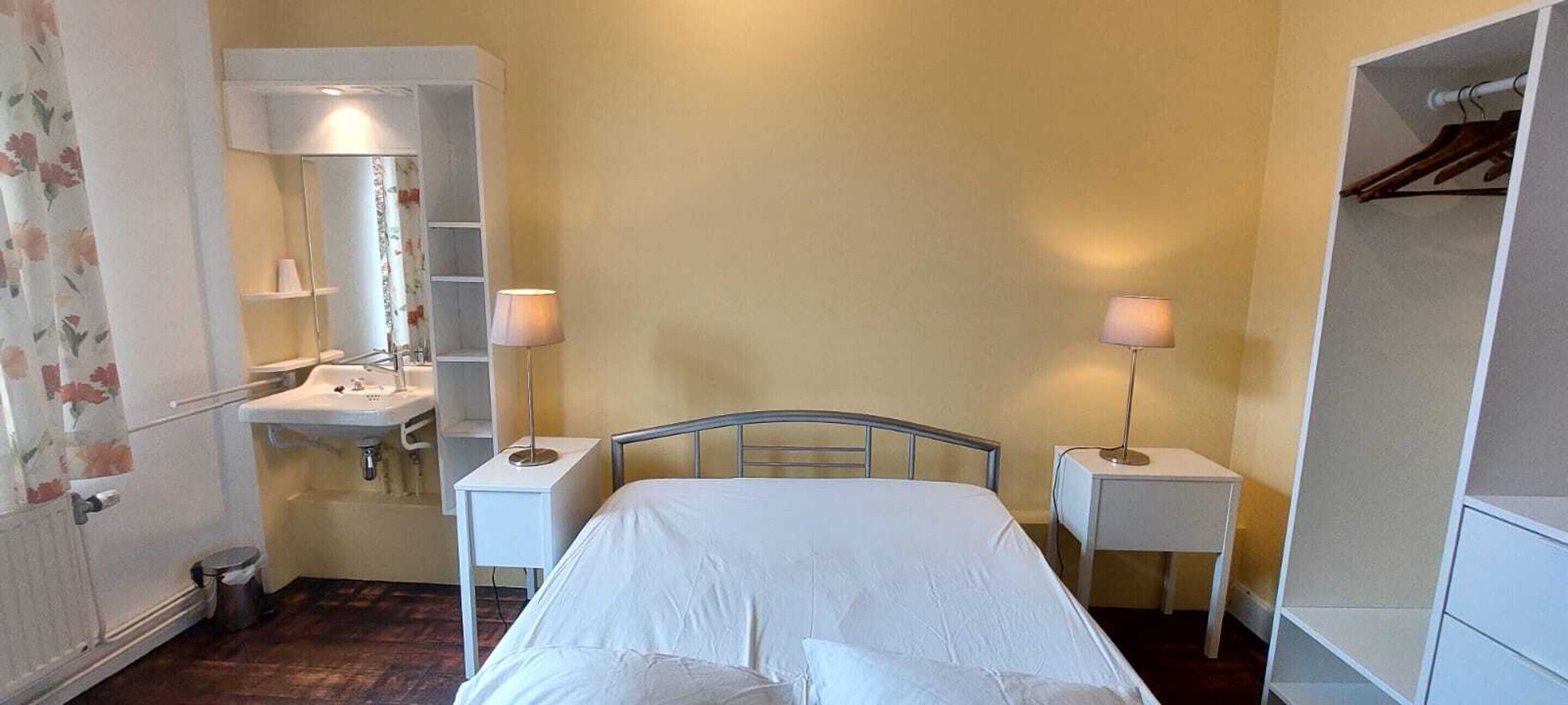 Un dormitorio pequeño y sencillo con cama, mesitas de noche, un espejo y un armario.