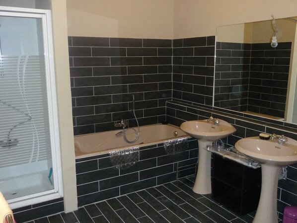 A bathroom with black tiled walls, a bathtub, two sinks, and a mirror. - Eco Hilltop Home in Falaen (Onhaye)