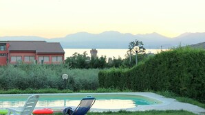 Une piscine avec des chaises longues et un grand flotteur rouge, entourée d’une haie et d’un bâtiment dont le toit est recouvert de tuiles.