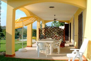 A covered patio with a table and chairs, a striped umbrella, and a lattice screen.