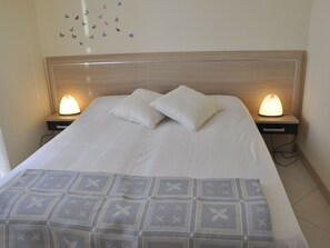 A neatly made bed with white linens and two pillows, flanked by bedside tables with lamps, in a room with a wooden headboard and a wall decorated with butterfly decals.