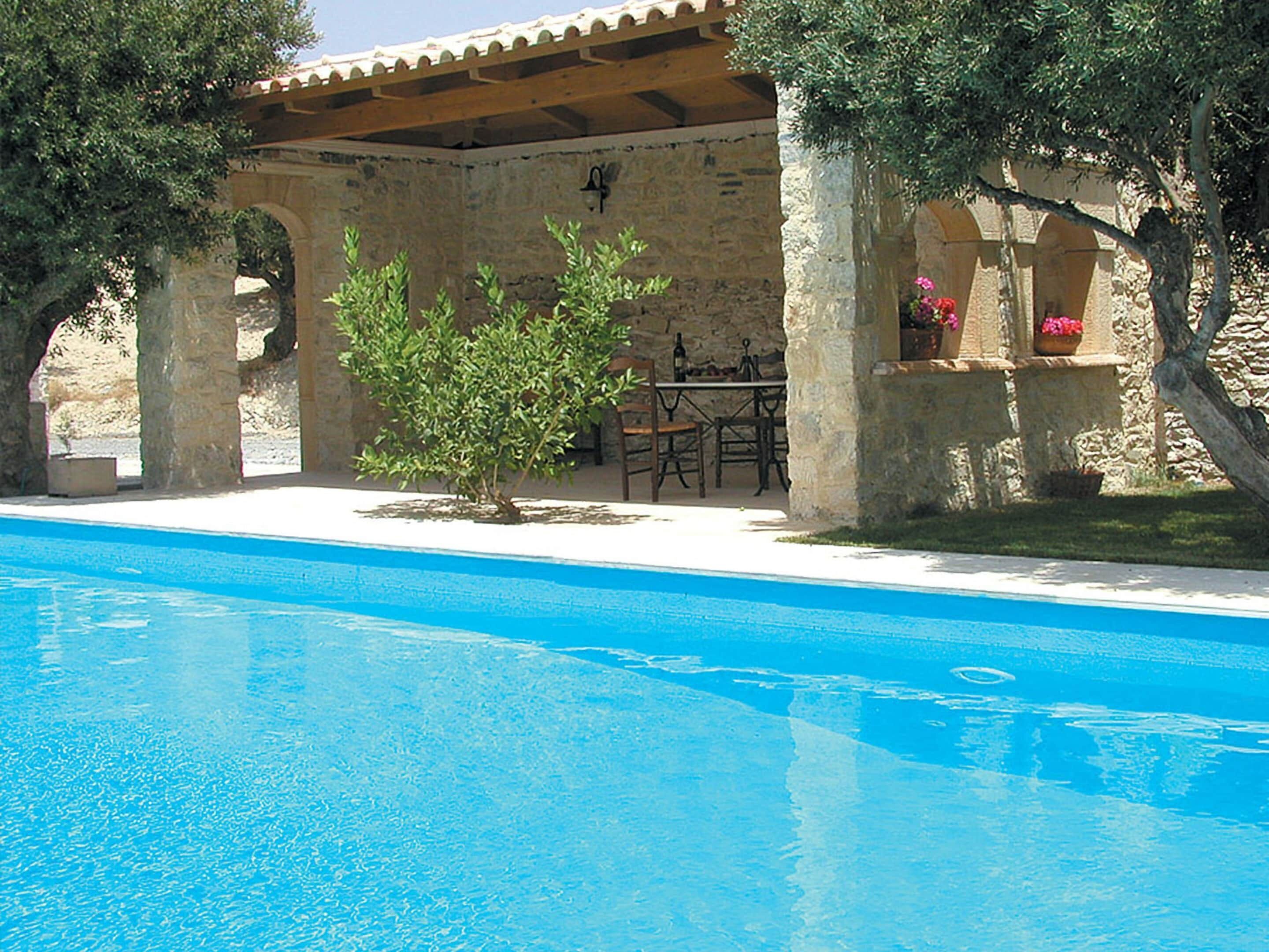 Una piscina con solarium in pietra, posti a sedere all'aperto e un pergolato.