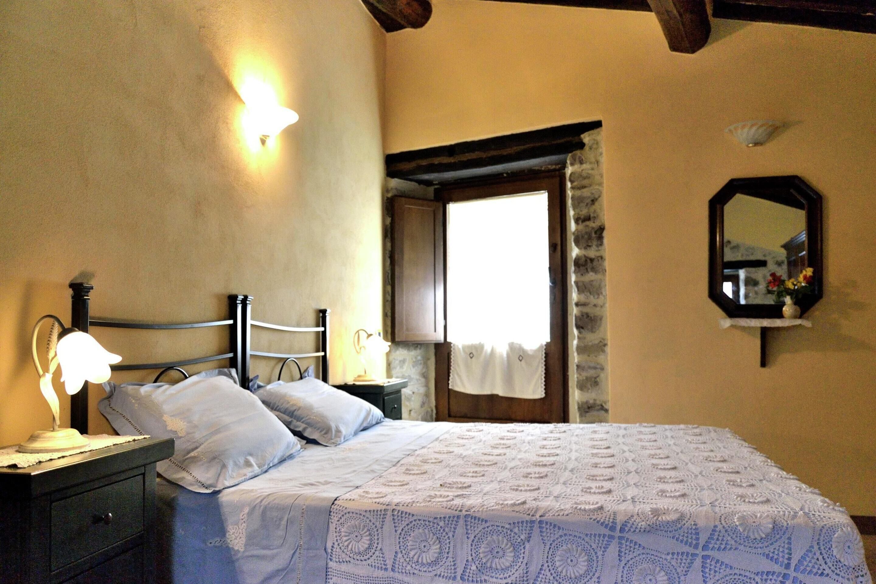 A bedroom with a bed, bedside tables, a lamp, a mirror, and a window with a curtain.