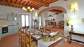 A rustic kitchen with a dining area, wooden beams, and a brick fireplace. - Holiday Home in Tuscany With Pool & Vineyards (Cortona)