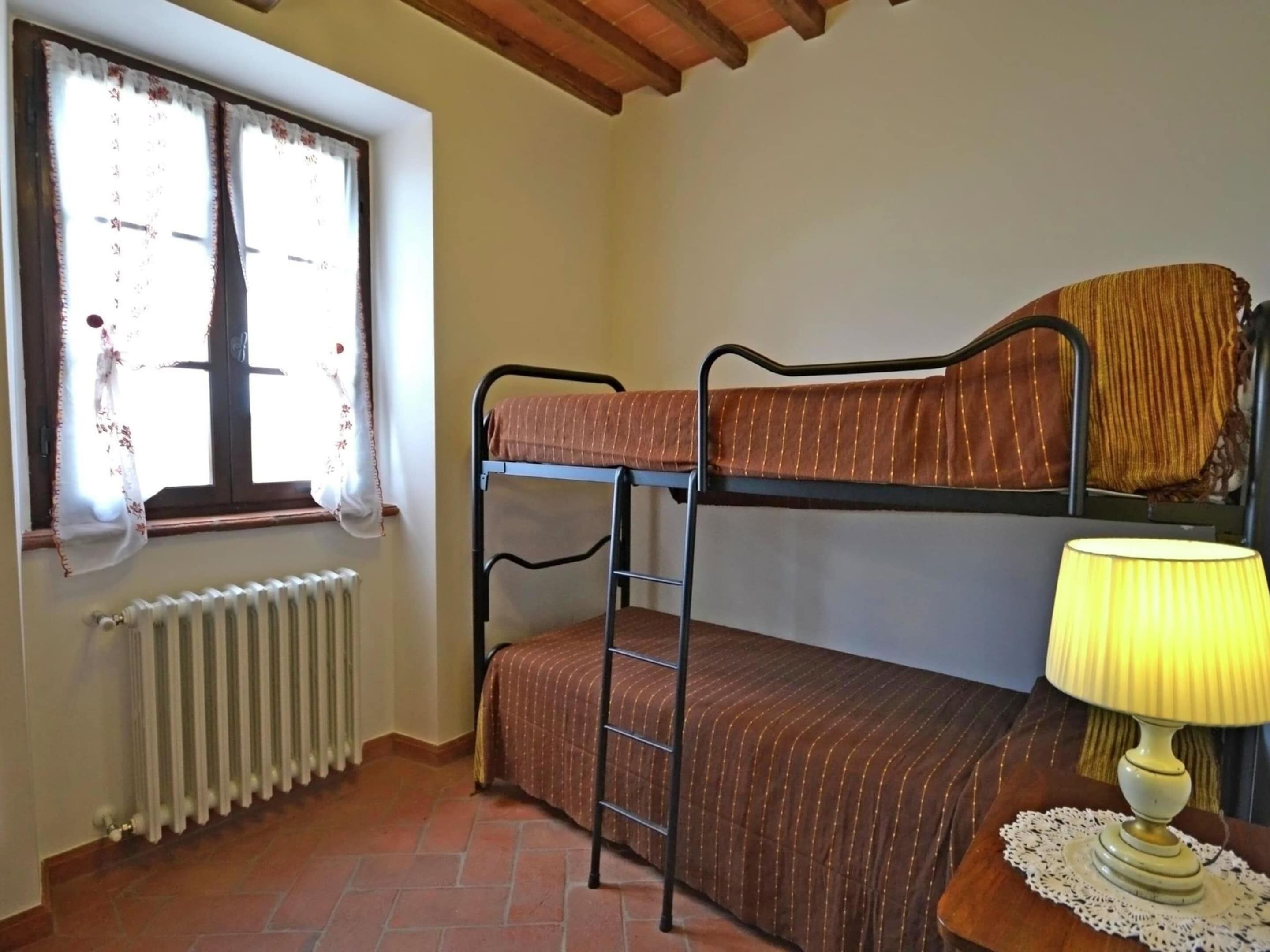 Ein Schlafsaalzimmer mit Etagenbetten, einem Heizkörper, einem Fenster mit Vorhängen und einer Nachttischlampe.