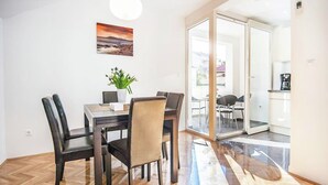 A dining area with a wooden herringbone floor, a table with chairs, a potted plant, and a painting on the wall. - Luxury Apartment With Private Balcony in Quiet Area (Dubrovnik)