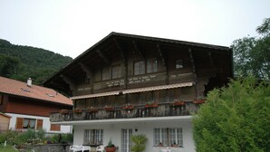 A traditional wooden building with a balcony, a gravel courtyard, and outdoor seating. - Pristine Home in a Charming Village, Large Grassy Sunbathing Area, View of the Mönch and Jungfrau (Wilderswil)