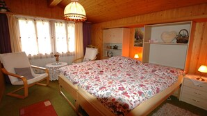 A bedroom with a wooden ceiling, a large bed with floral bedding, two chairs, a small table, and a dresser. - Pristine Home in a Charming Village, Large Grassy Sunbathing Area, View of the Mönch and Jungfrau (Wilderswil)