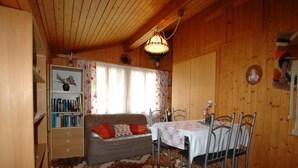 A cozy room with a wooden ceiling, a sofa with cushions, a dining table with chairs, and a bookshelf. - Pristine Home in a Charming Village, Large Grassy Sunbathing Area, View of the Mönch and Jungfrau (Wilderswil)