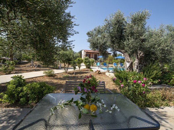 A glass table with a vase of flowers, a pool, and a building in the background.