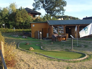 A wooden cabin with a small patio, a flag, and a golf course in the background. - Apartment in Heringhausen Near Ski Lift (Diemelsee)