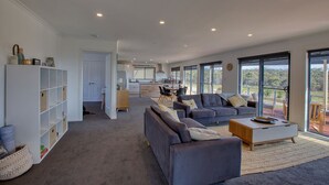 Un vaste espace de vie comprenant un grand canapé, une table basse et une bibliothèque. Au fond, on aperçoit une cuisine avec un coin repas.