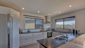 Une cuisine moderne avec des meubles blancs, un grand îlot central doté d’un évier, d’une cuisinière et d’une fenêtre offrant une vue sur l’extérieur.