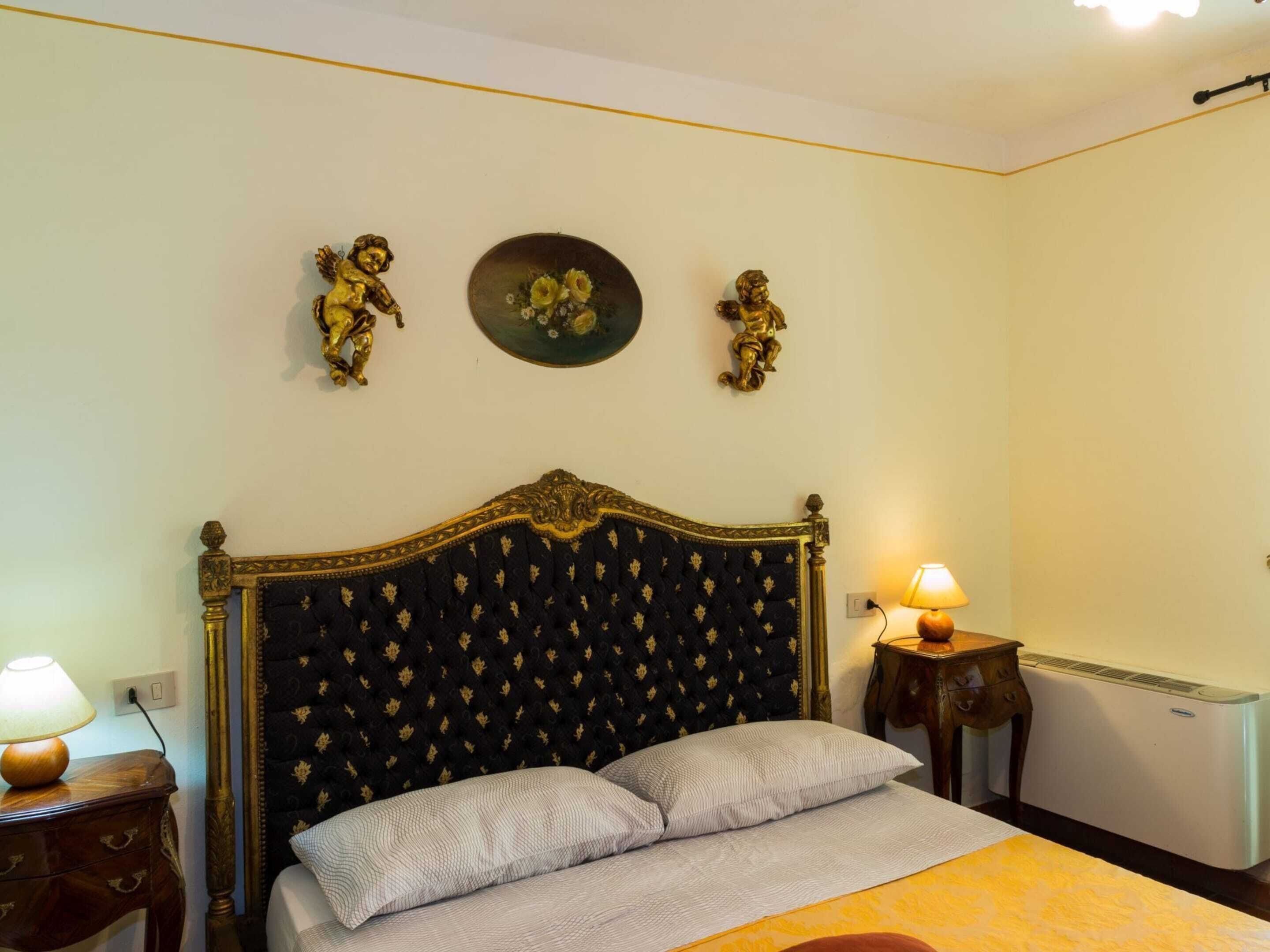 A bedroom with a large bed, two bedside lamps, a radiator, and decorative angel figurines on the wall.