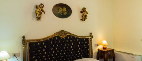 A bedroom with a large bed, two bedside lamps, a radiator, and decorative angel figurines on the wall.