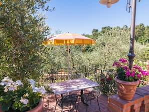 An outdoor patio with a table and chairs, surrounded by potted plants and an umbrella.