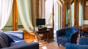 A cozy living room with a television on a wooden table, blue armchairs, and a brick wall. - Nice Farmhouse in Montecatini Terme with Sauna & Hot Tub (Pieve a Nievole)