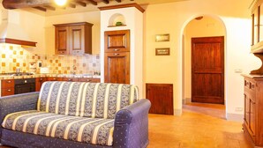 A cozy living room with a sofa, wooden cabinets, and a tiled backsplash in the kitchen area. - Belvilla by OYO Mimosa (Cortona)