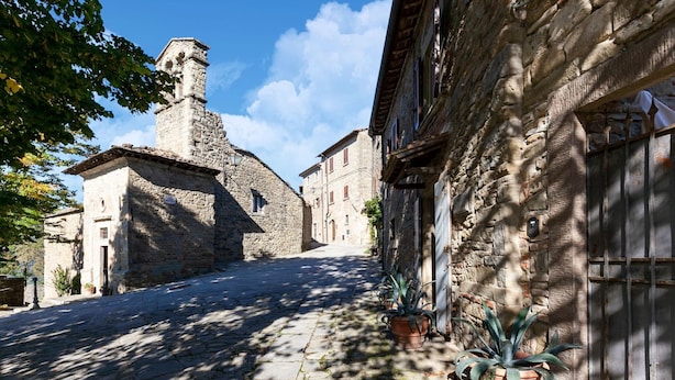 A narrow cobblestone street flanked by stone buildings with traditional architecture, including a prominent tower. - Belvilla by OYO Mimosa (Cortona)