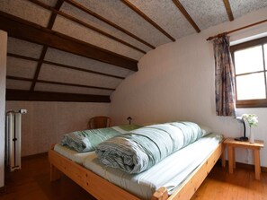 A small, cozy bedroom with a wooden bed, a wooden nightstand, a window with curtains, and a radiator. - Tranquil Holiday Home in Houffalize With Barbecue (Houffalize)