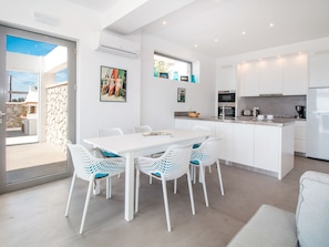 A modern kitchen with white cabinetry, a central island, and a dining area with white chairs.
