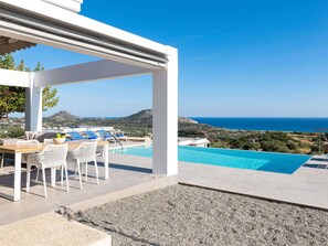 A poolside area with a pergola, outdoor seating, and a view of the sea.