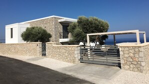 A modern house with a stone facade, a gated entrance, and a view of the sea.