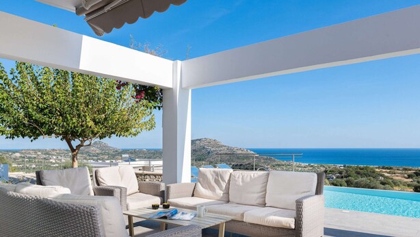 A covered outdoor seating area with wicker furniture, a pool, and a view of the sea and landscape. - Sea View Villa in Kalythies with Private Pool near 3 Beaches (Rhodes)
