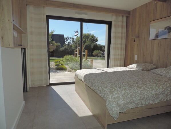 A bedroom with a bed, a sliding glass door leading to a garden, and wooden paneling on the walls. - Seaside house, 400 m from the beach, with fiber optics. (Plouarzel)